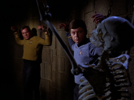 Kirk, McCoy, and a skeleton chained to the wall of a dark dungeon
