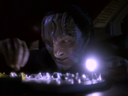 Garak in a darkened room holding a flashlight over a kotra board game