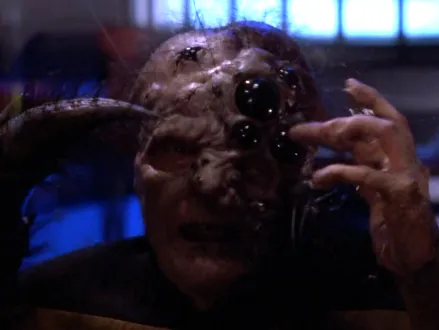 A part-human part-spider with one hand and one large claw and several eyes on one side of its head