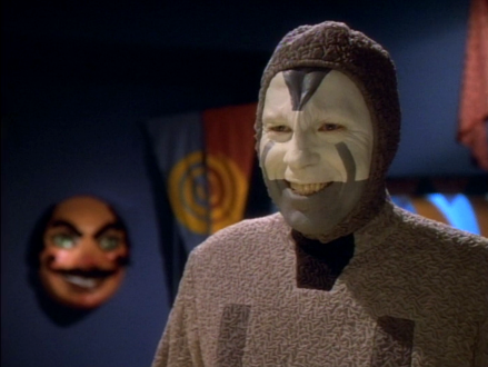 A clown wearing a grey suit with white and grey makeup