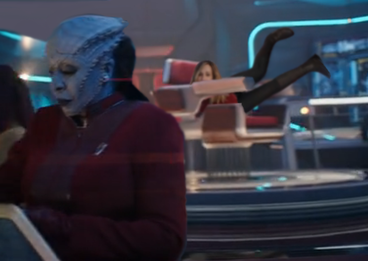 Lura Thok in the foreground, with Captain Ake in the background, peeking over the armrest of her Captain's chair, with her legs nearly straight up in the air