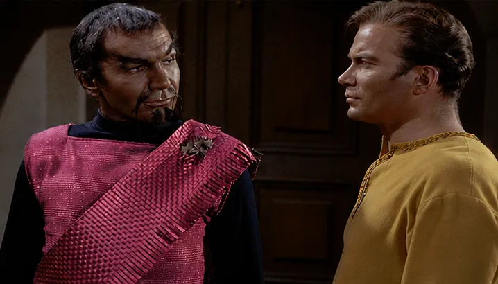 Captain Kirk speaking with the Klingon Kor, who is wearing a pink uniform