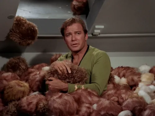 Kirk standing in a small mountain of small, furry creatures known as tribbles