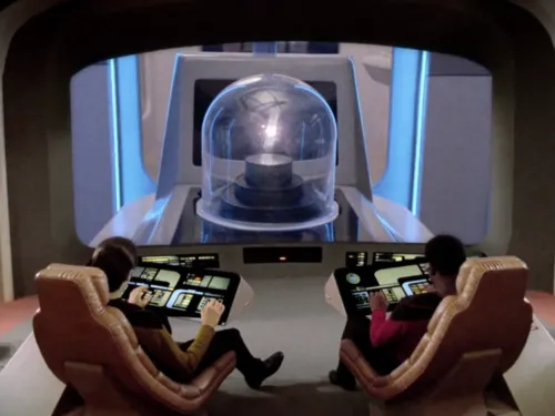 Data and Geordi observing on the bridge viewscreen a lifeform which is a small point of light under a glass dome in a lab