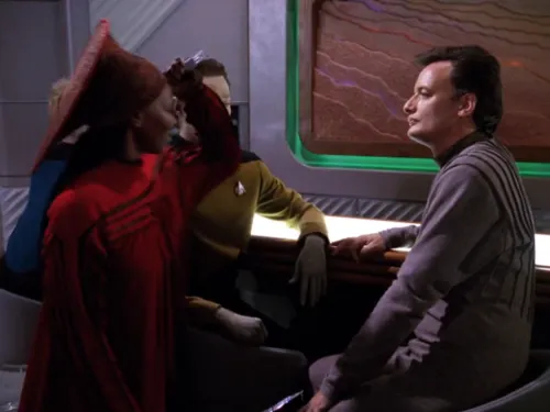Guinan lifting a fork in the air, preparing to stab Q's hand with it