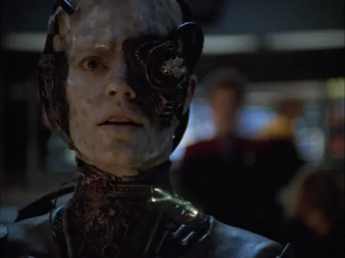 A fully-Borg Seven of Nine looking shocked with Janeway lurking in the background