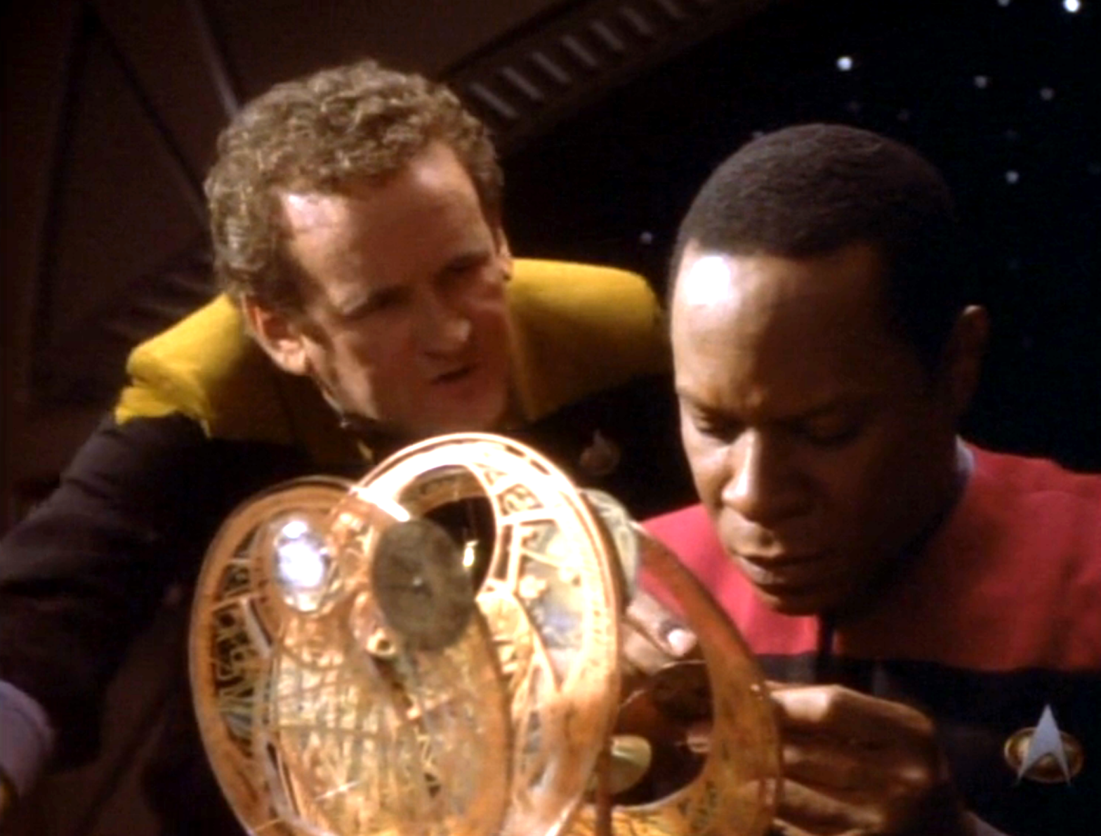 O'Brien leaning over Sisko as he builds a clock