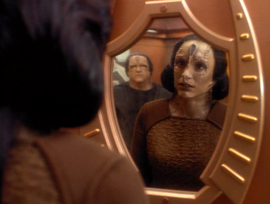 Kira, altered to look like a Cardassian, staring at herself in a mirror while another Cardassian watches