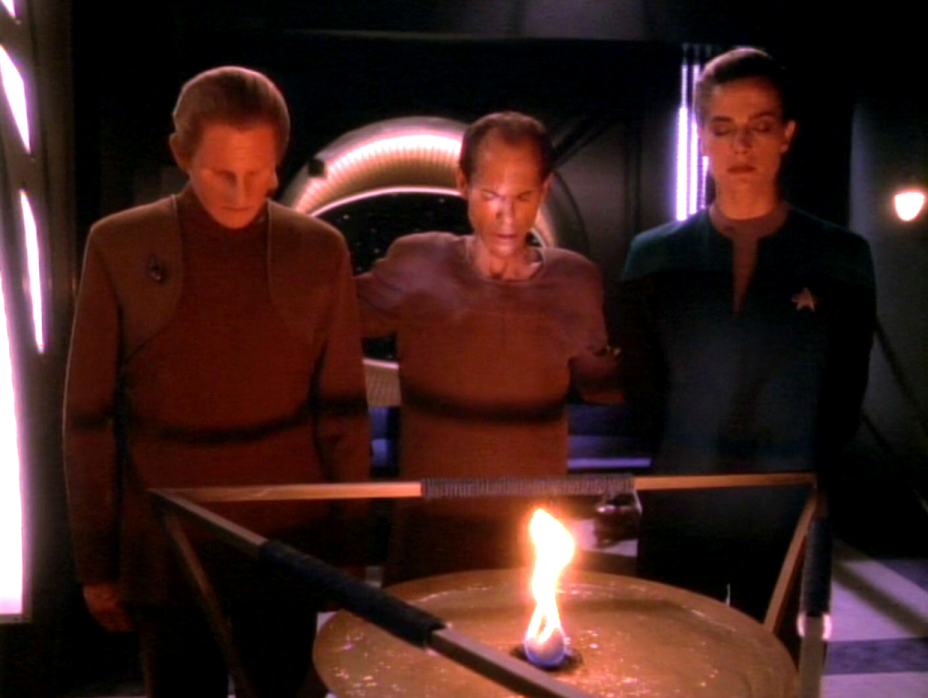 Odo, Dax, and another man standing with their eyes closed in front of an altar with a flame