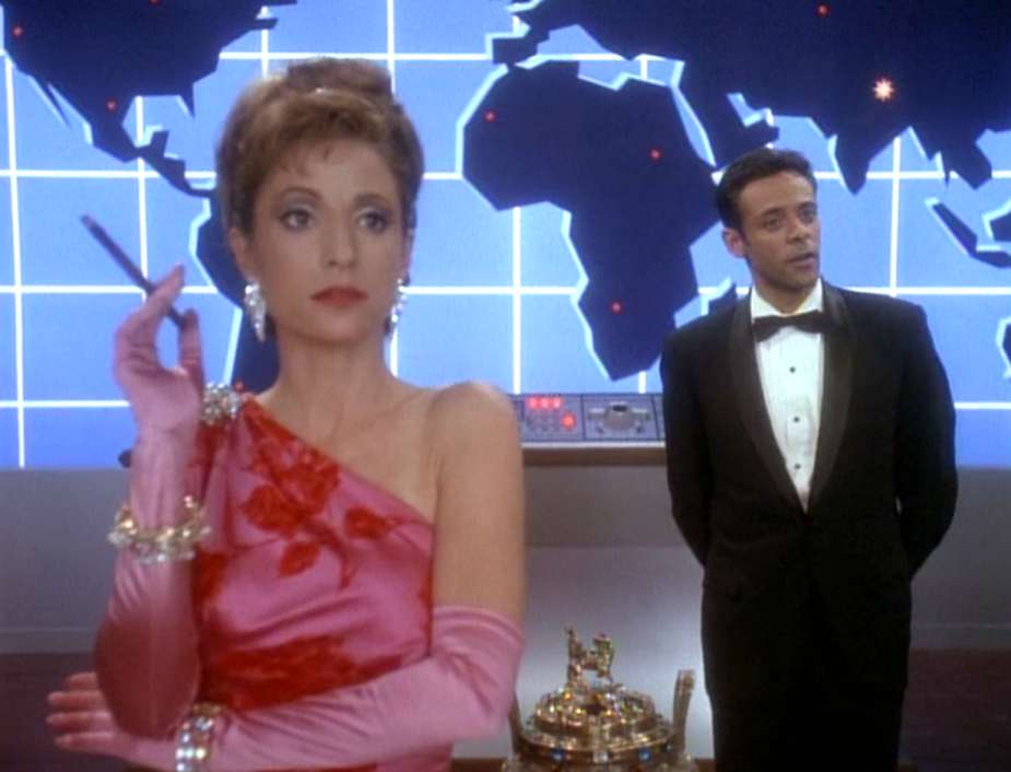 Kira in a dress and Bashir in a tuxedo standing in front of a world map