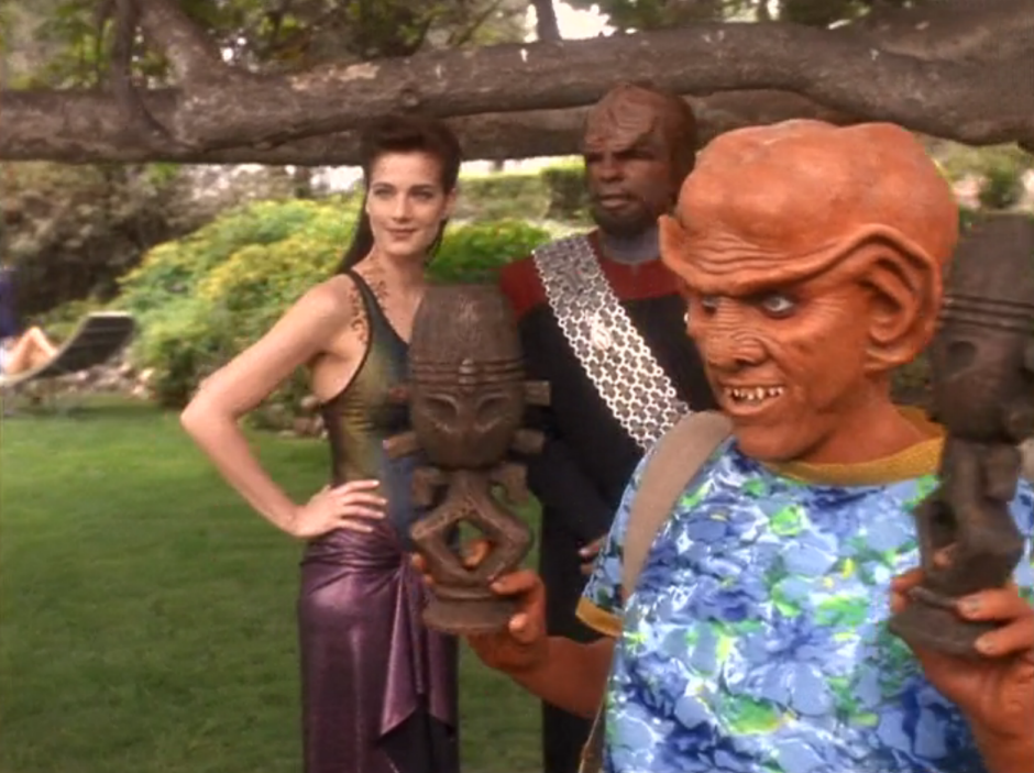 Quark holding two horga'hn statues with Worf and Dax in a grassy area on Risa