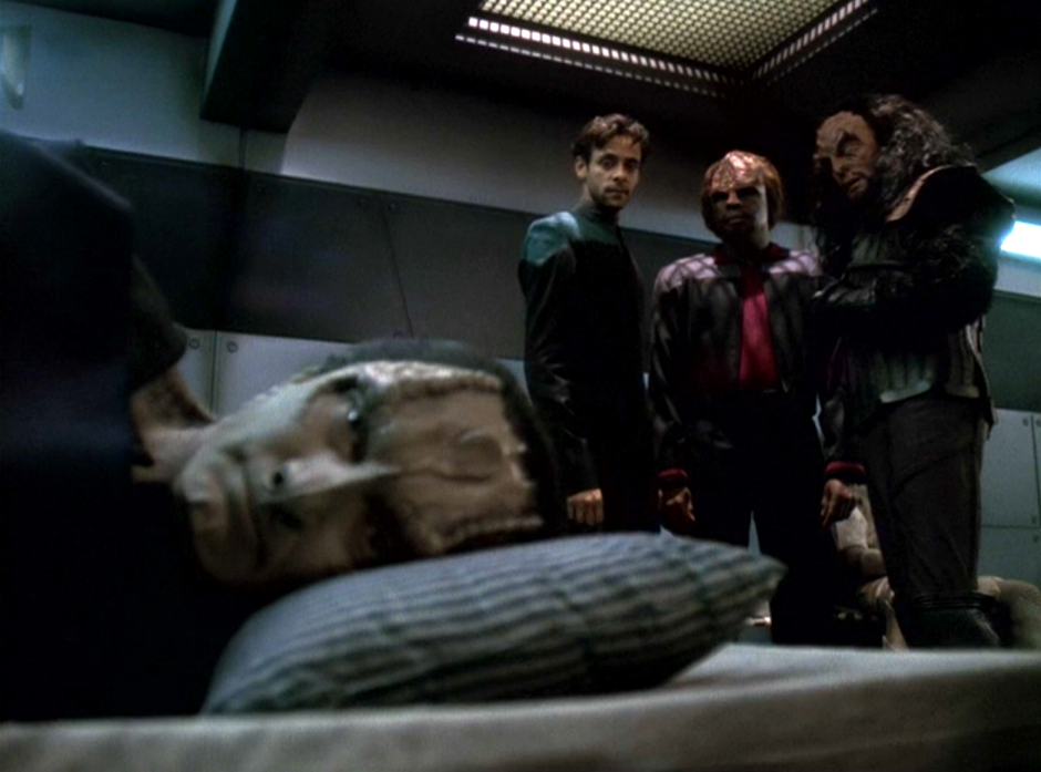 Garak lying down and looking ill as Bashir, Worf, and Martok look on