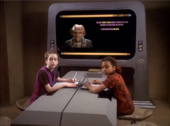 An image of Quark on a computer screen teaching a lesson to two school children