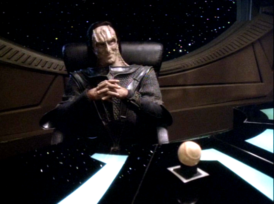 Dukat sitting with his fingers interlaced behind Sisko's desk