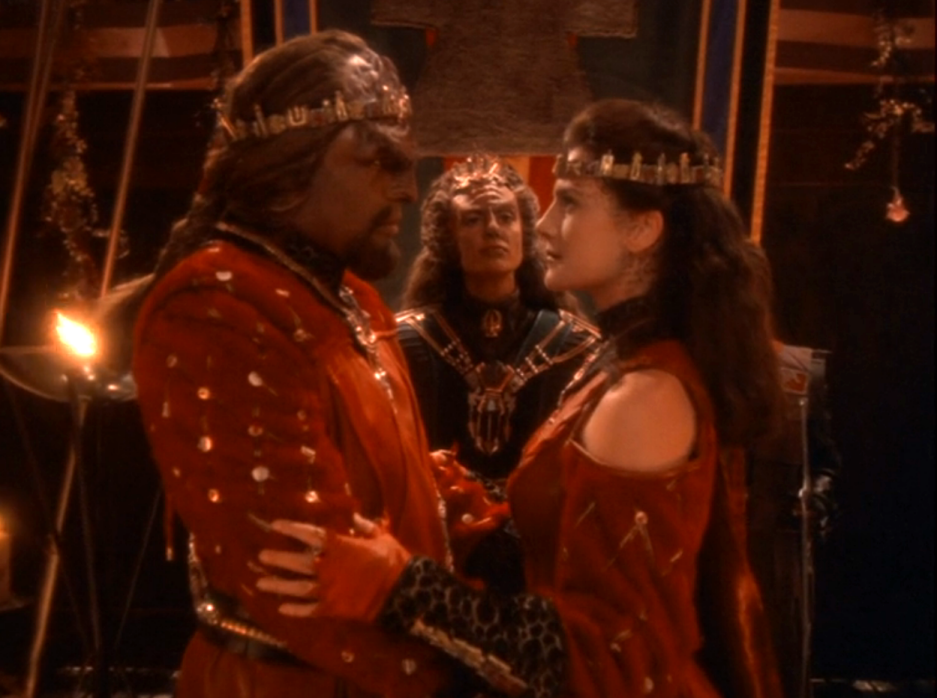 Worf and Jadzia wearing crowns and red clothing starring into each other's eyes