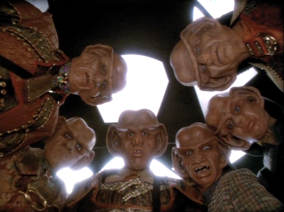 Six Ferengi in a circle staring down directly into the camera