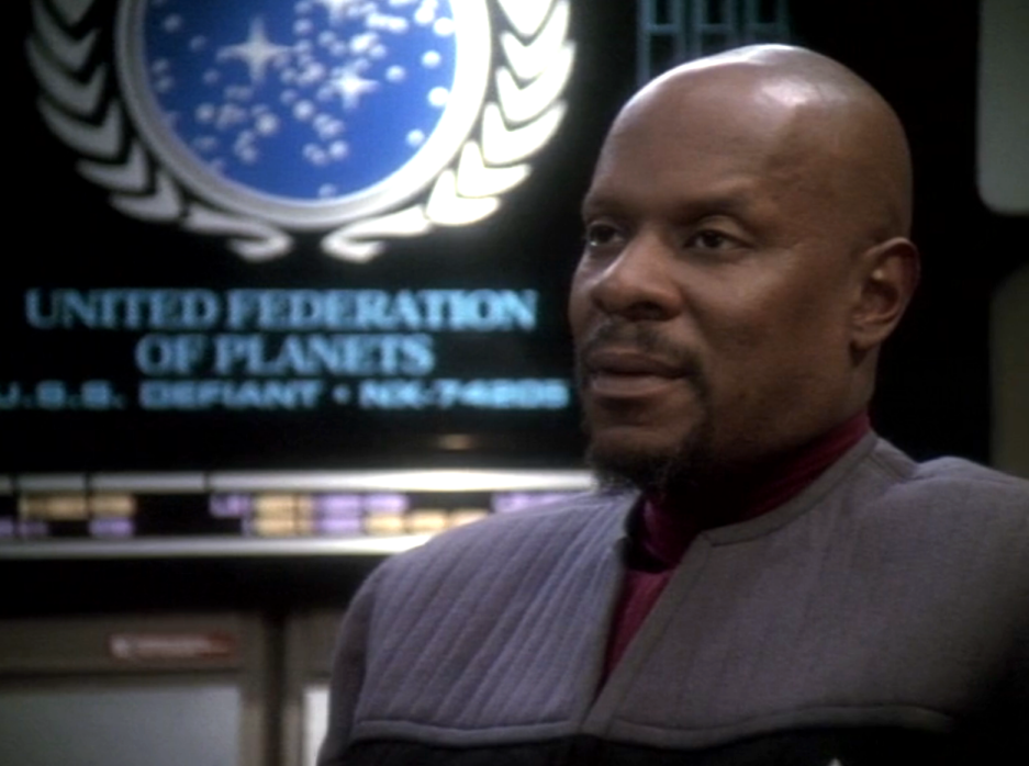 Sisko sitting in front of the United Federation of Planets seal