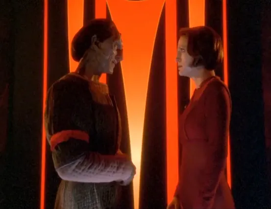Dukat wearing a red arm-band and talking face-to-face with Kira