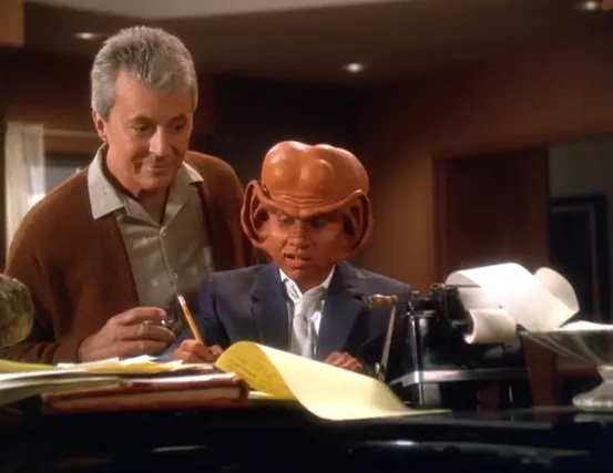 Nog using paper, pencil, and an adding machine as Vic looks over his shoulder approvingly