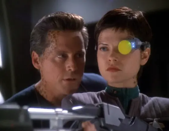 Ezri aiming a rifle as another Trill looks over her shoulder