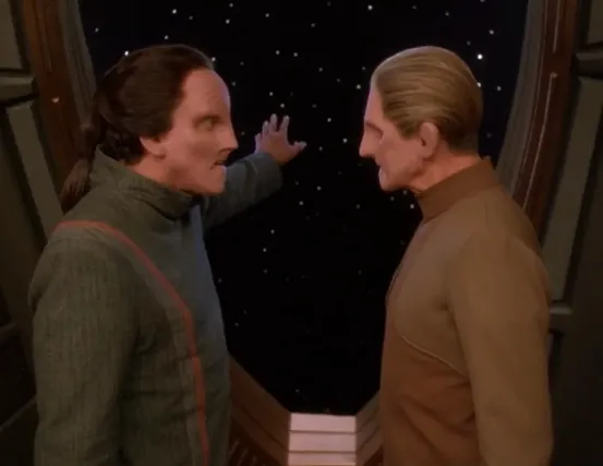 A changeling gesturing out the window as he talks to Odo
