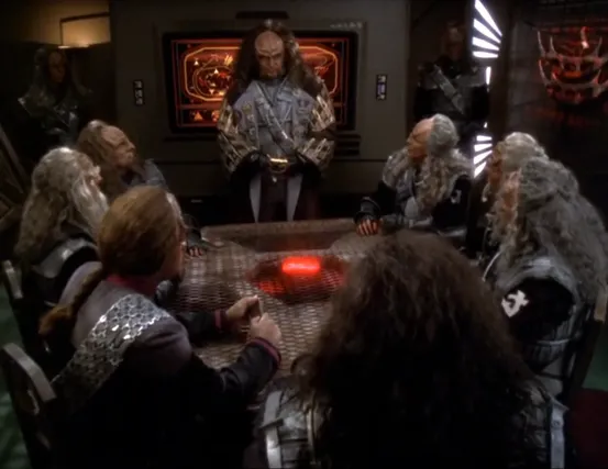 Gowron discussing battle plans at the head of a conference table surrounded by other Klingons