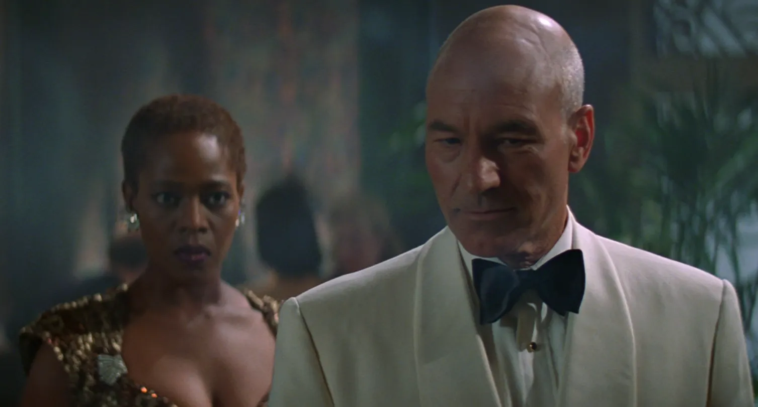 Lily wearing a satin dress and Picard in a white suit in a smoky ballroom