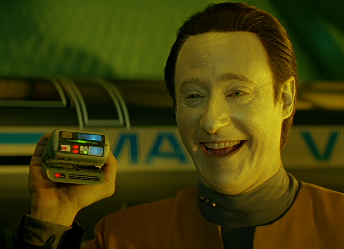 Data smiling and holding up a tricorder like a puppet