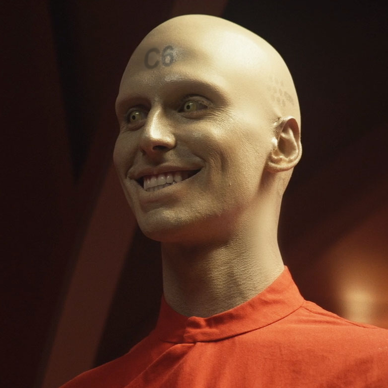 a smiling, pale-skinned android with C6 tattooed to his forehead