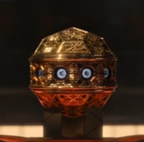 An intricate orb with many sides, golden in color, with circular blue-white lights around the middle