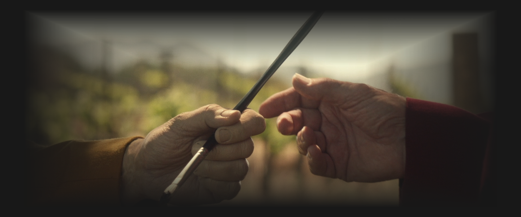 a pale-white hand with a yellow sleeve giving a paintbrush to another hand with a red sleeve