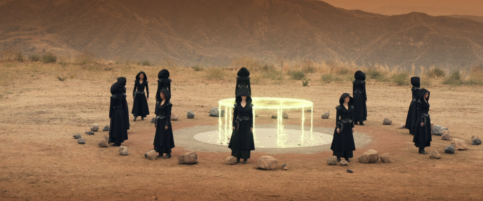 Eleven black-hooded figures stand around a glowing altar on a dusty planet