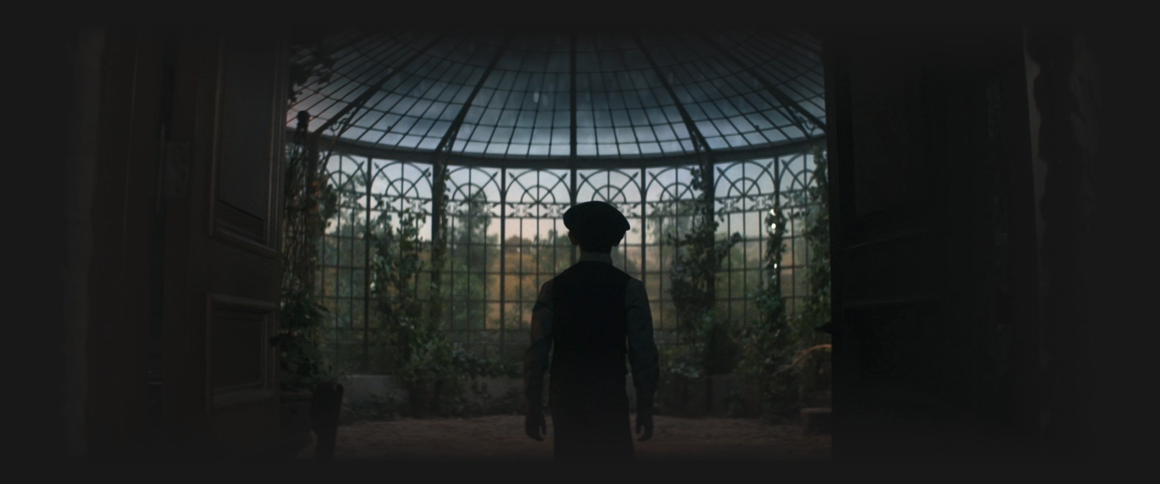 A young boy with a beret entering a large solarium