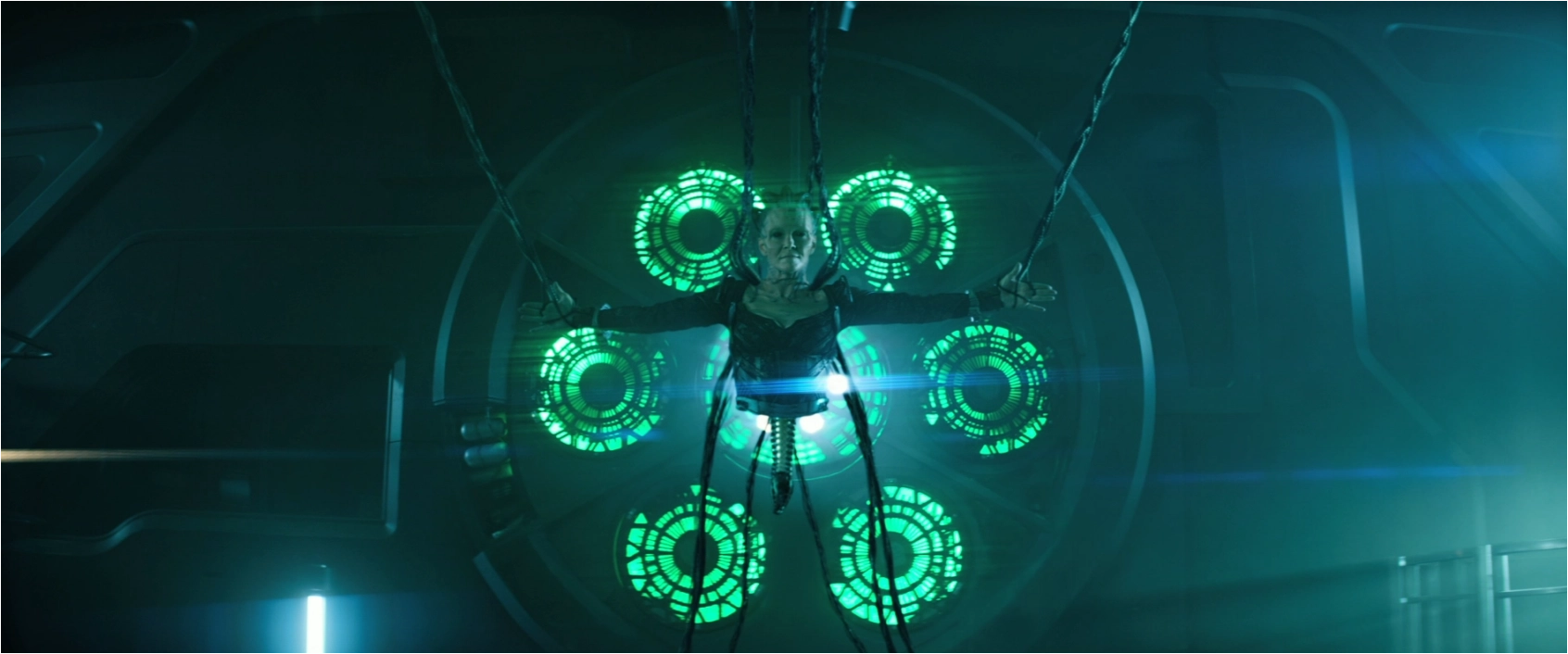A legless Borg Queen suspended from the ceiling with green glowing lights behind her