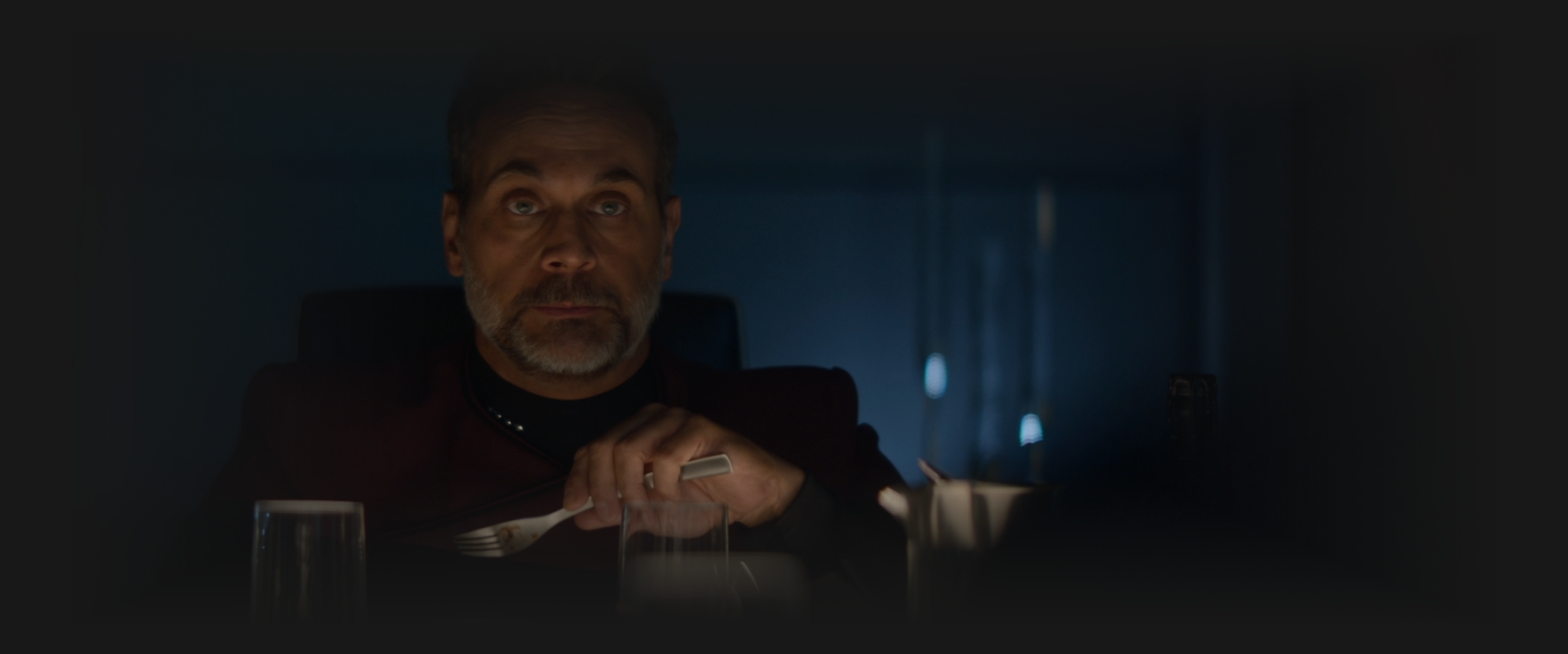 Captain Shaw at a dinner table looking annoyed