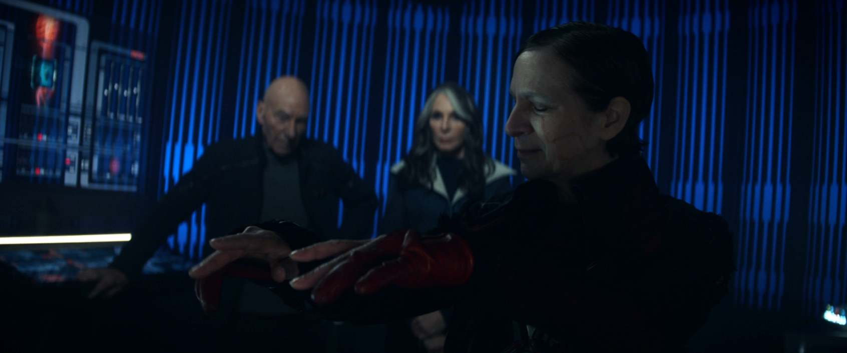 Vadic, slightly smiling and wiggling her fingers as if to music, while Picard and Crusher observe