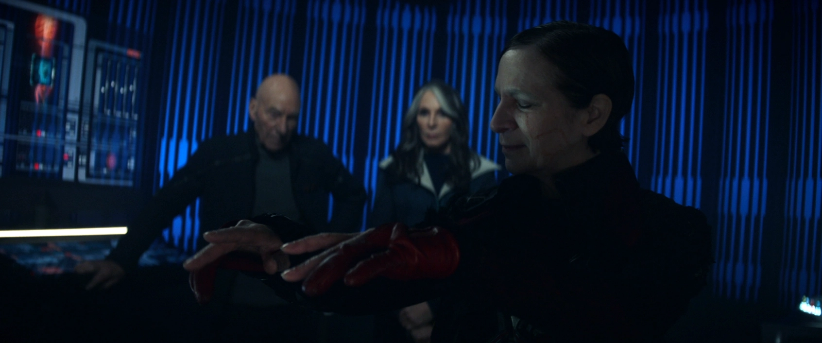 Vadic, slightly smiling and wiggling her fingers as if to music, while Picard and Crusher observe