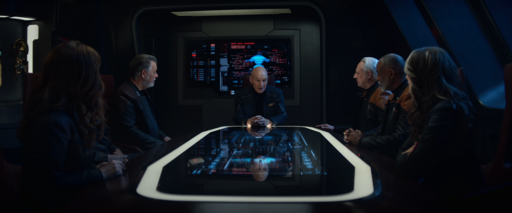 A photo of Picard, Riker, Worf, Troi, Data, La Forge, and Crusher, all sitting around a conference table, but Troi is blocking the camera's view of Worf