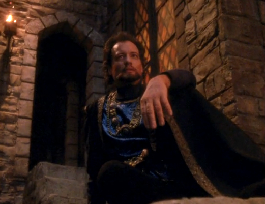 Q, in a Medieval-era outfit, posing as the Sheriff of Nottingham