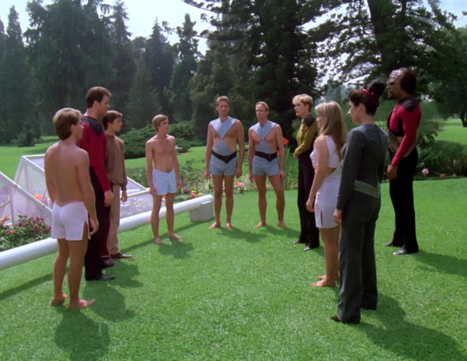 Members of the Enterprise crew speaking with several of the scantily-clad Edo in a pleasant garden