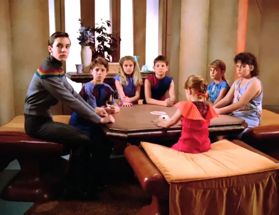 Wesley sitting around a table with six other children from the Enterprise