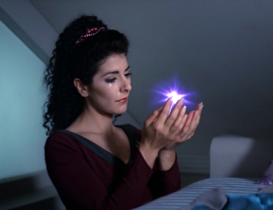 Troi, cradling a spark of light, with a tear in her eye