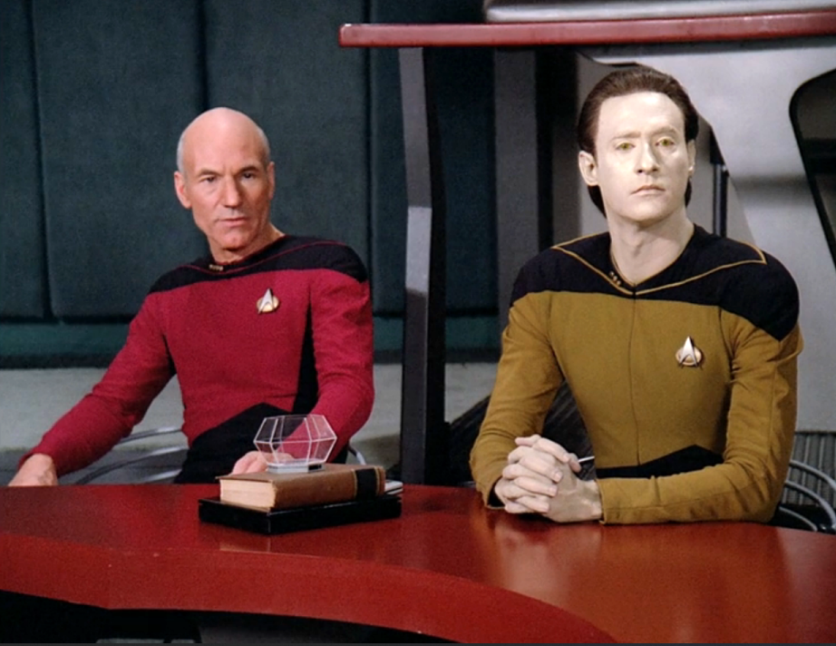 Picard and Data sitting at a table in a courtroom
