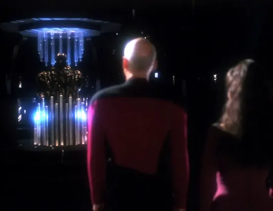 Picard and Troi standing before the Sheliak representative