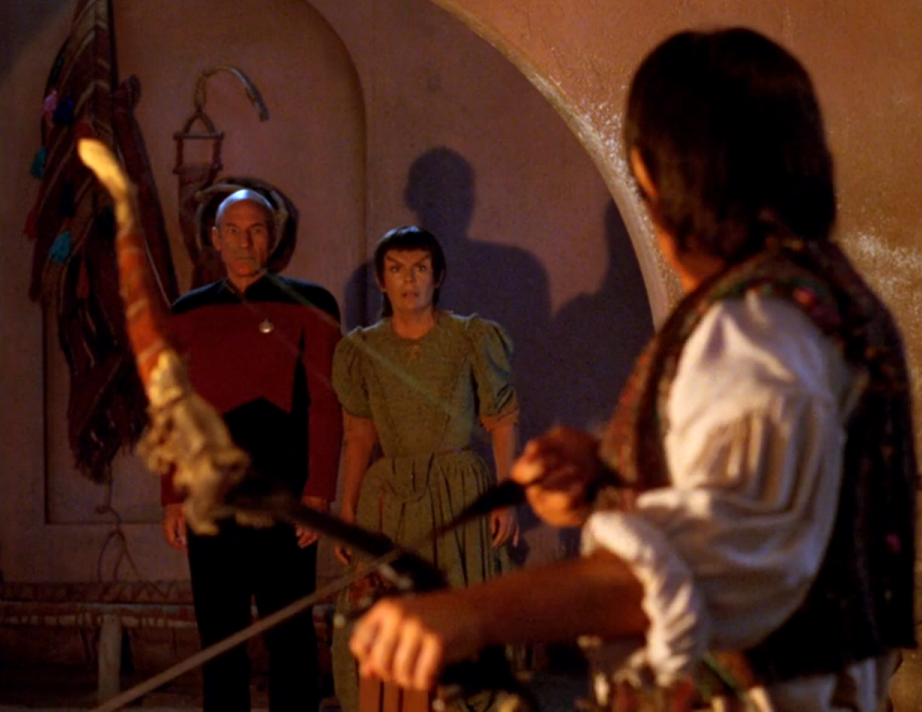 Liko lowering his bow and arrow as Picard and Nuria arrive