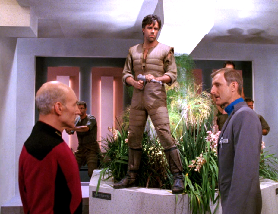 Soldiers holding a room of people at gunpoint, including Picard