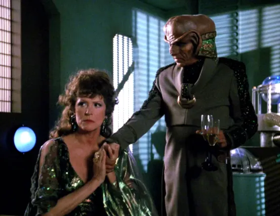 An annoyed-looking Lwaxana Troi holding the hand of a lecherous Ferengi