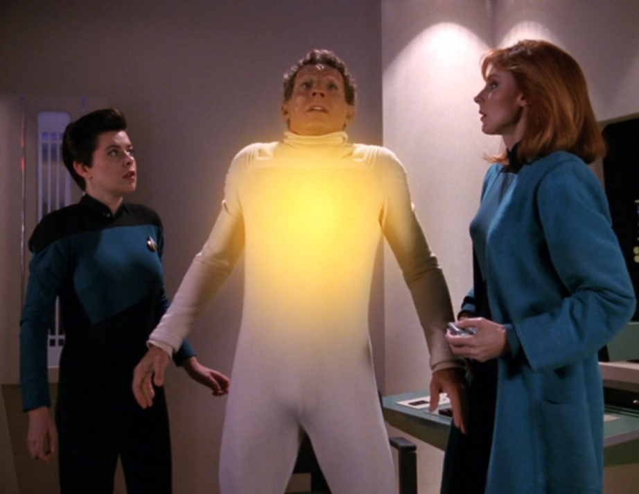 Dr. Crusher watches as a bright yellow glow emanates from her patient's chest