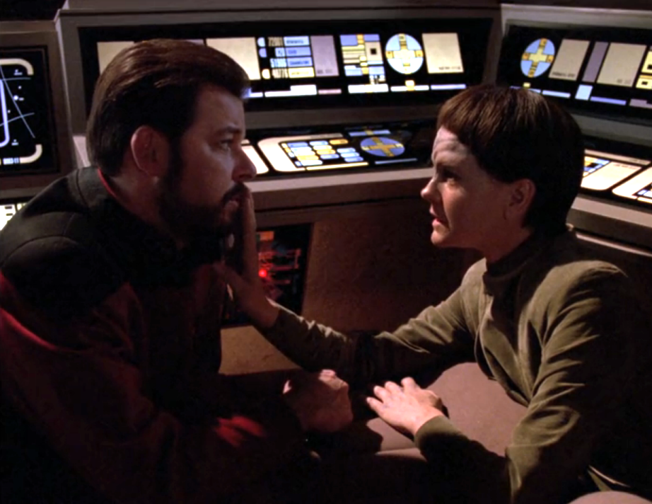 An androgynous alien reaching out to hush Riker as they have a conversation in a shuttlecraft