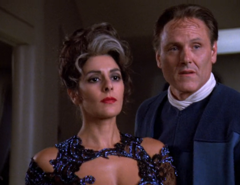 Deanna Troi, with an up-do and streak of grey in her hair, with an alien man